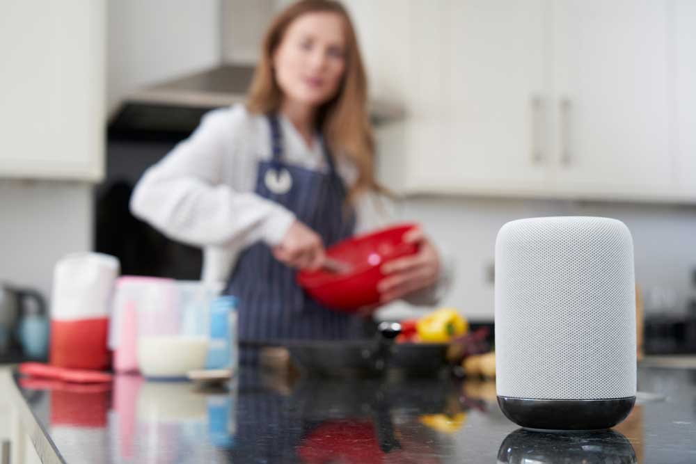 A woman asks a digital assistant a question in her kitchen