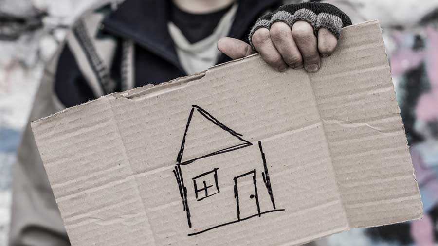 Homeless person holds cardboard showing a picture of a house