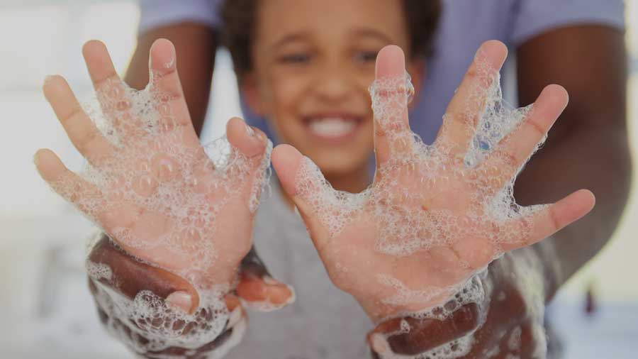 A smiling child holds up soapy hands