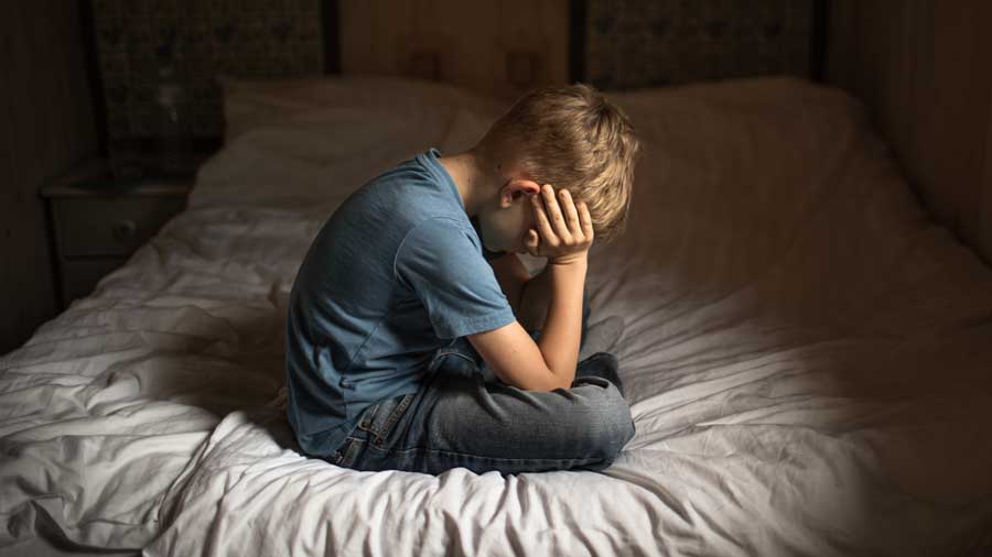A sad boy sits on a bed