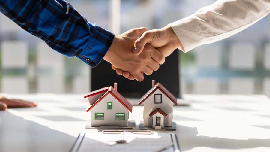 Two people shake hands in agreement over a model of two houses