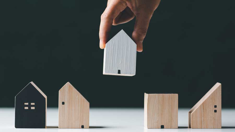 A hand places a model house among other houses