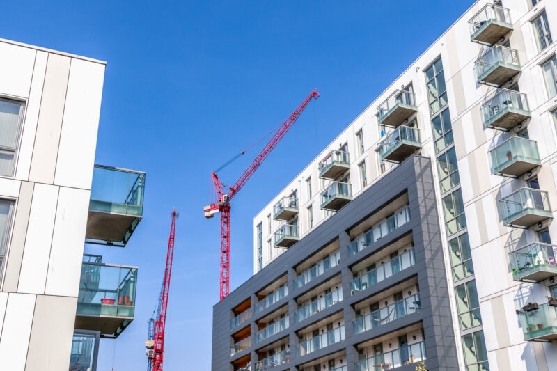 Facade of a modern flat with building cranes in the background indicating new development