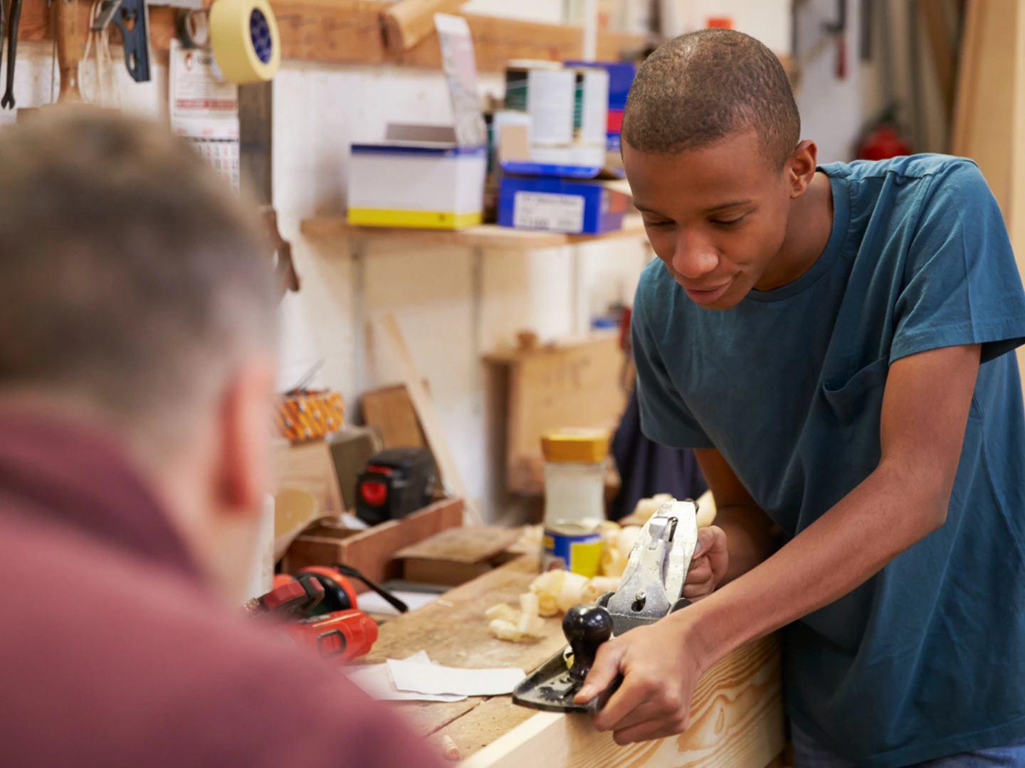 Carpenter With Apprentice Planing Wood In Workshop stock photo