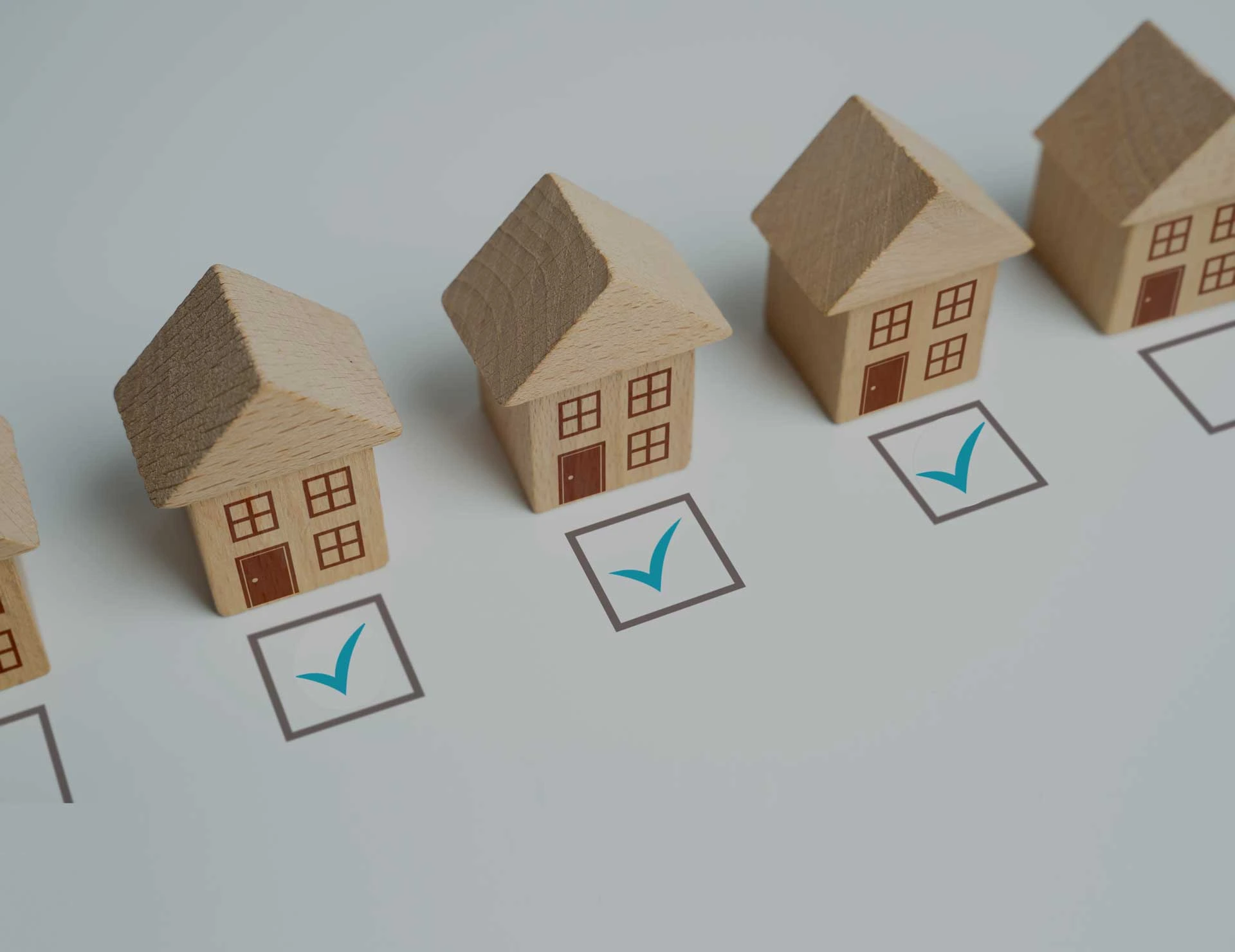 A group of wooden houses in a row with check boxes beneath them. One house has a green tick in the check box.